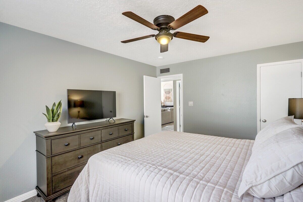 A bedroom with a bed, a dresser, a television, and a ceiling fan.