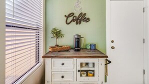 A kitchen with a coffee-themed decor, including a wall sign, a coffee maker, and a basket with a plant.