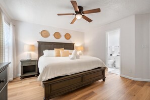 A bedroom with a large bed, wooden headboard, bedside lamps, and a ceiling fan.