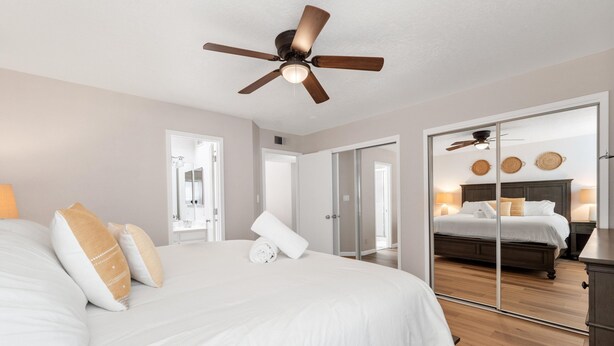 A bedroom with a large bed, a ceiling fan, and a mirrored closet door.
