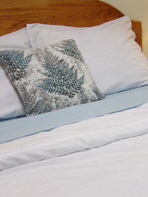 Uma cama com roupa de cama branca e almofada estampada.
