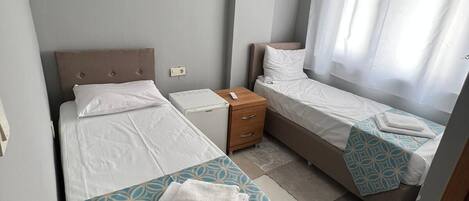 A hotel room with two beds, a bedside table, a small wooden cabinet, and an air conditioning unit.