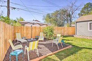 Ein Garten mit Holzzaun, einer Terrassenfläche mit gestreiften Stühlen und einem Tisch sowie ein kleines Gartenhaus.