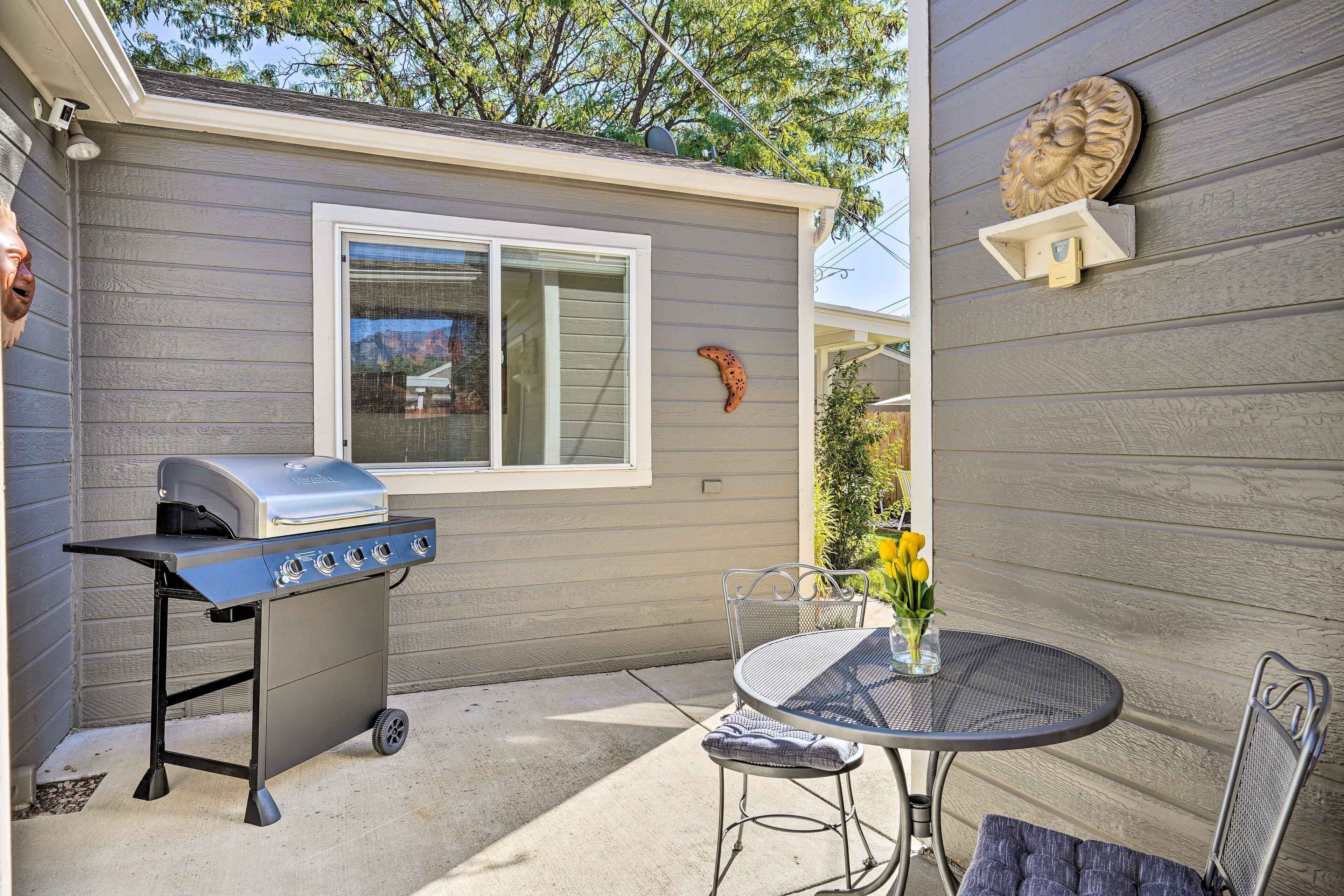 A patio with a grill, a table with chairs, and a decorative wall piece.