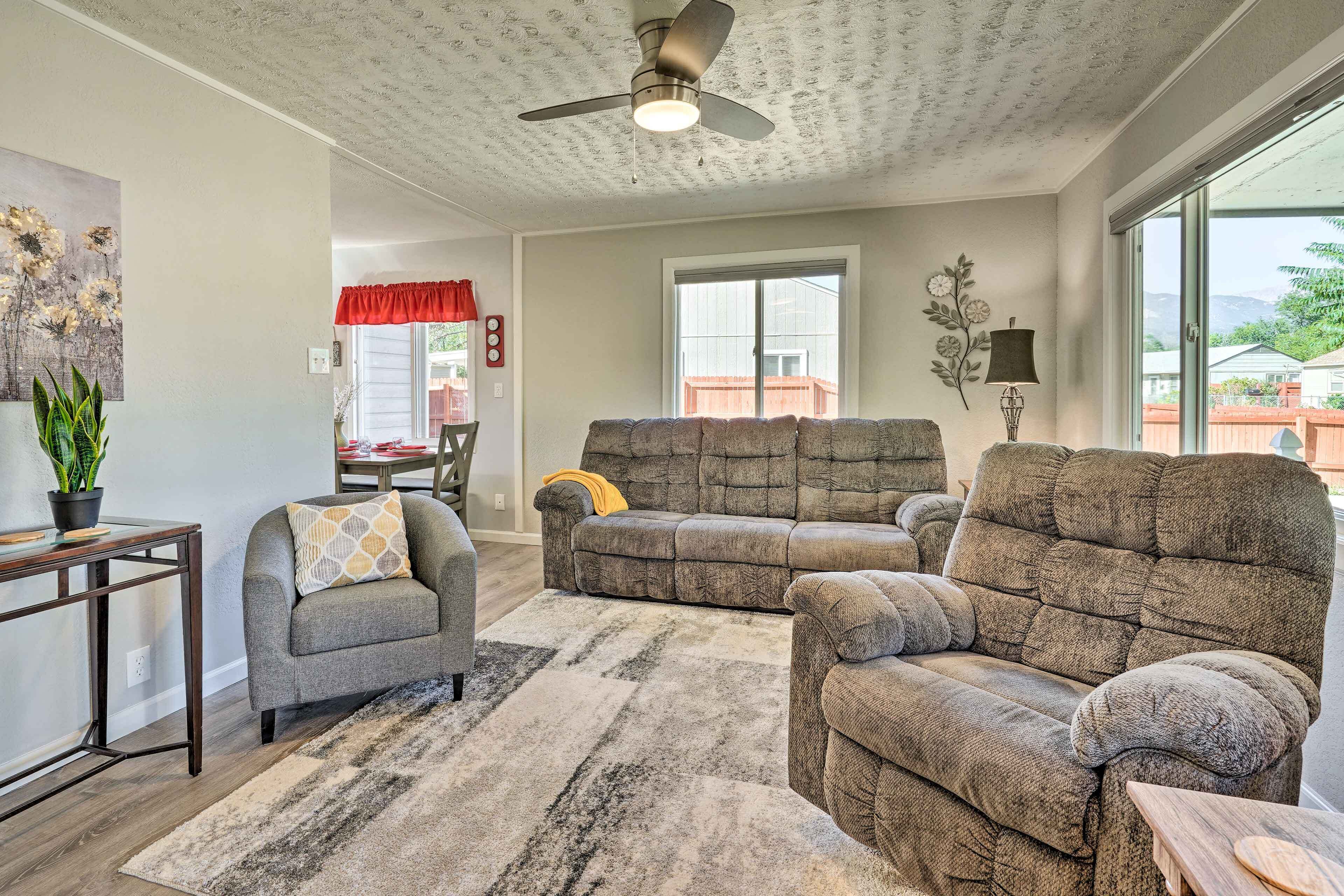 A living room with a ceiling fan, a gray sofa, a small armchair, and a large window.