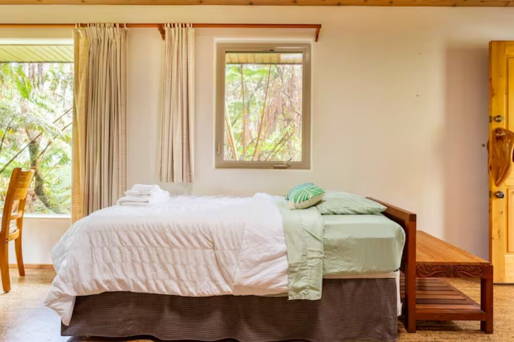 Um quarto com uma cama, uma janela, uma porta de madeira e uma cadeira.