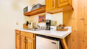 Eine kleine Küche mit Holzschränken, einer weißen Arbeitsplatte, einer Kaffeemaschine und einem kleinen Kühlschrank.