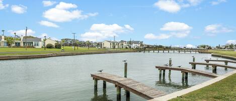 A waterfront area with a dock, calm water, and residential buildings in the background.