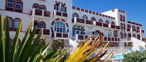 A multi-story hotel with balconies, large windows, and a pool area.