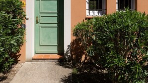 Ein Gebäude mit einer grünen Tür, einem kleinen Fenster mit weißem Rahmen und einem größeren Fenster mit weißem Rahmen und geöffneten Fensterläden.