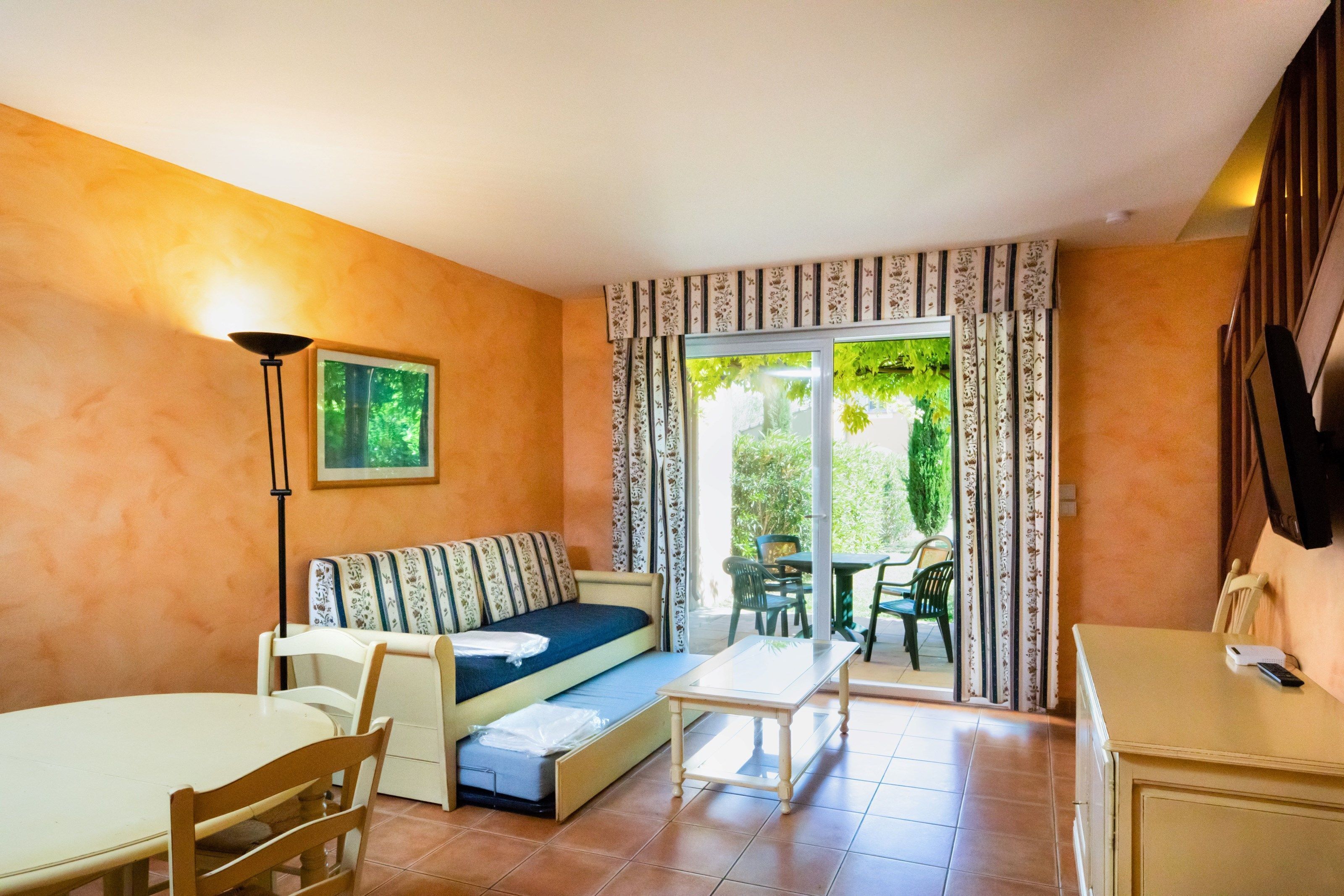 Une pièce confortable avec un canapé, une table à manger et des chaises. Une porte-fenêtre coulissante donne accès à un espace extérieur agrémenté de verdure.