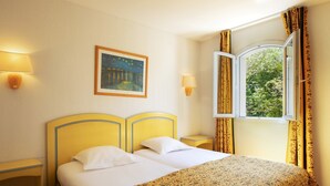 Ein Hotelzimmer mit einem Bett, zwei Nachttischen, einem Schrank, einem Bild, einem Fenster mit Vorhängen und Blick auf Grünfläche.
