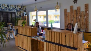 A reception desk with wooden panels, a large window, and a wall-mounted wooden rack with keys. - Escapade à Grandcamp av/Piscine, Sauna et Wifi (Grandcamp-Maisy)