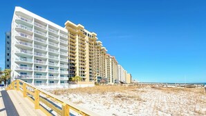 Ein Strandhotel mit mehreren Balkonen, einer Holzpromenade und einem Sandstrand.