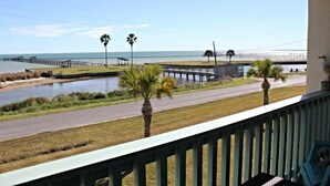 A view from a balcony overlooking a coastal area with a road, a small water body, and a distant pier. - Golden Gull by Miss Kitty’s (Rockport)