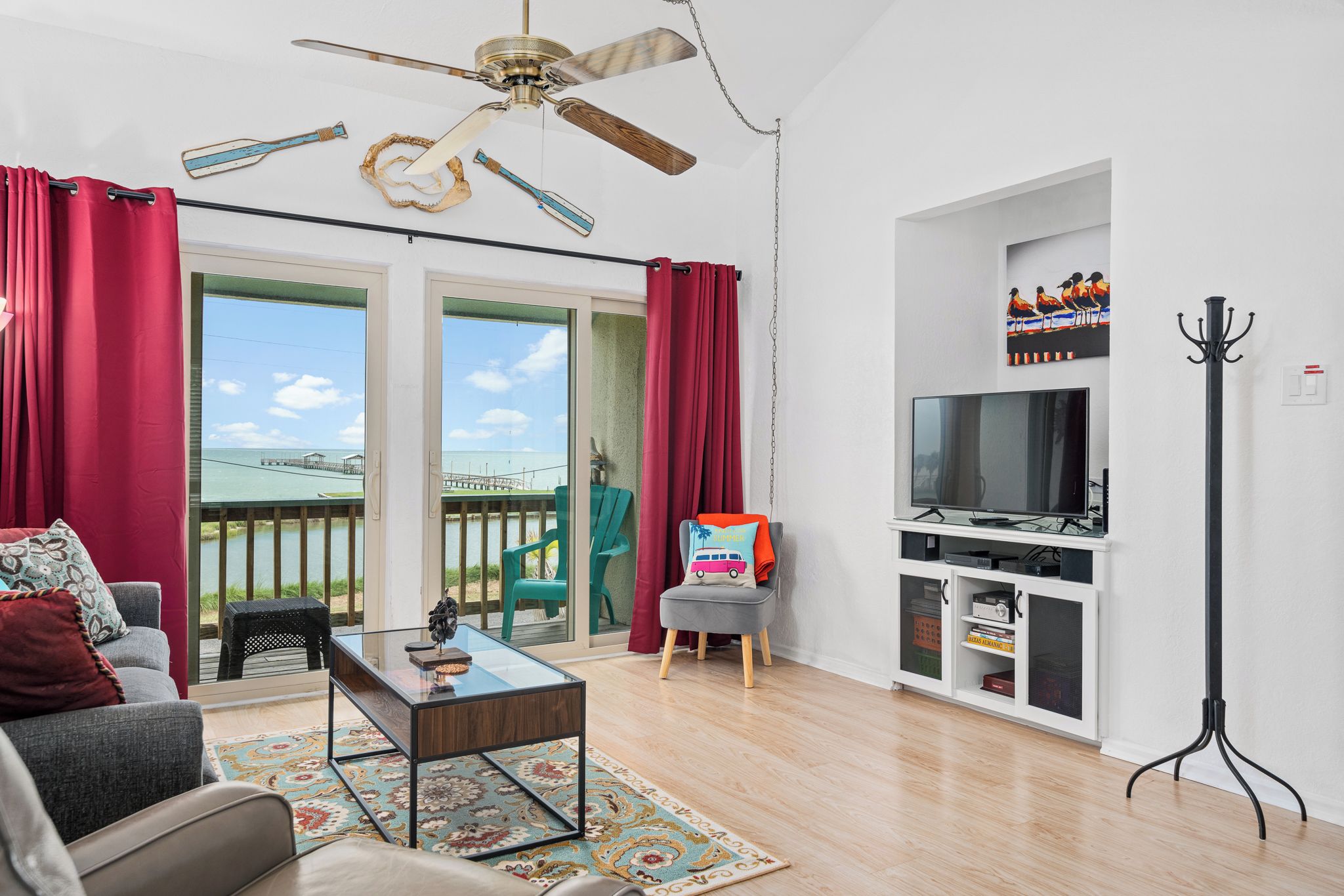A living room with a TV, a ceiling fan, a glass coffee table, a sofa, and a view of the outdoors.