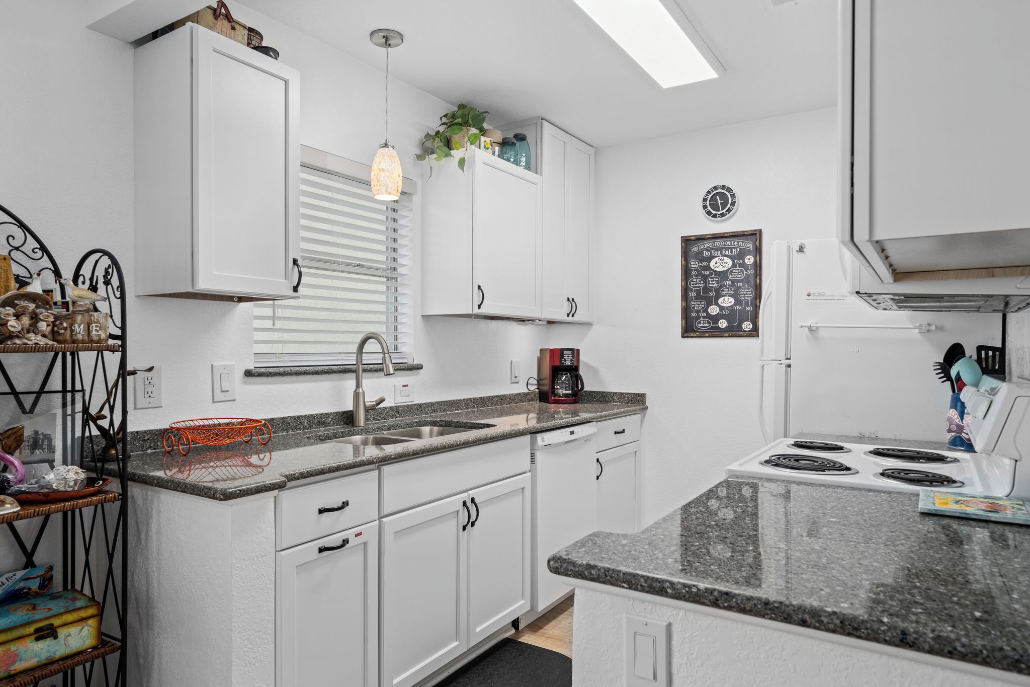 A modern kitchen with white cabinets, a granite countertop, a built-in stove, and a coffee maker.