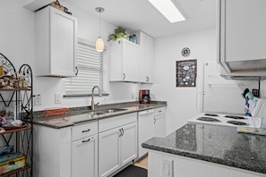 A modern kitchen with white cabinets, a granite countertop, a built-in stove, and a coffee maker. - Golden Gull by Miss Kitty’s (Rockport)