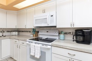 A kitchen with white cabinets, a microwave, a stove, a coffee maker, and a knife block.