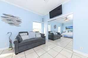 A spacious living room with a grey sofa, a second sofa, a flat-screen TV, and a large window.