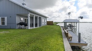Ein Wassergrundstück mit überdachter Terrasse, Grill und einer anlegenden Mole.