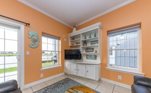 A living room with a TV, white cabinets, and decorative items on shelves.