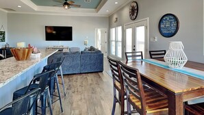A modern kitchen with a bar area, a large TV, and a dining space with wooden chairs and a table.