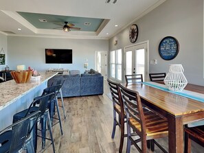 A modern kitchen with a bar area, a large TV, and a dining space with wooden chairs and a table. - Tequila Sunset by Miss Kitty’s (Rockport)