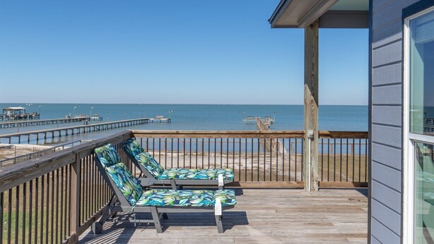 A wooden deck with two lounge chairs facing a beach and pier.