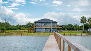 A two-story waterfront property with a wooden dock leading to a house with balconies.
