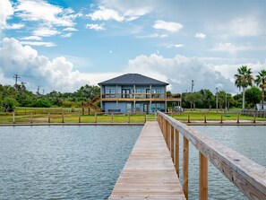 A two-story waterfront property with a wooden dock leading to a house with balconies. - Tequila Sunset by Miss Kitty’s (Rockport)