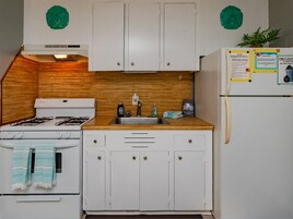 A compact kitchen with white cabinets, a gas stove, a sink, and a refrigerator. There are two green decorative plates on the wall above the cabinets.