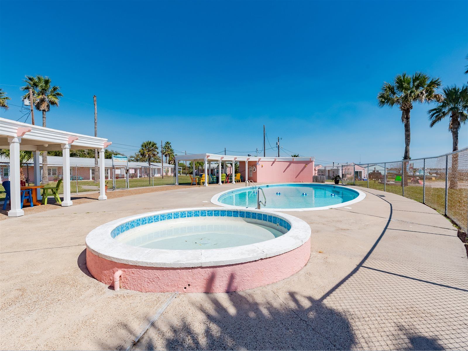 Un área de piscina con dos piscinas circulares, un espacio de descanso techado y palmeras.