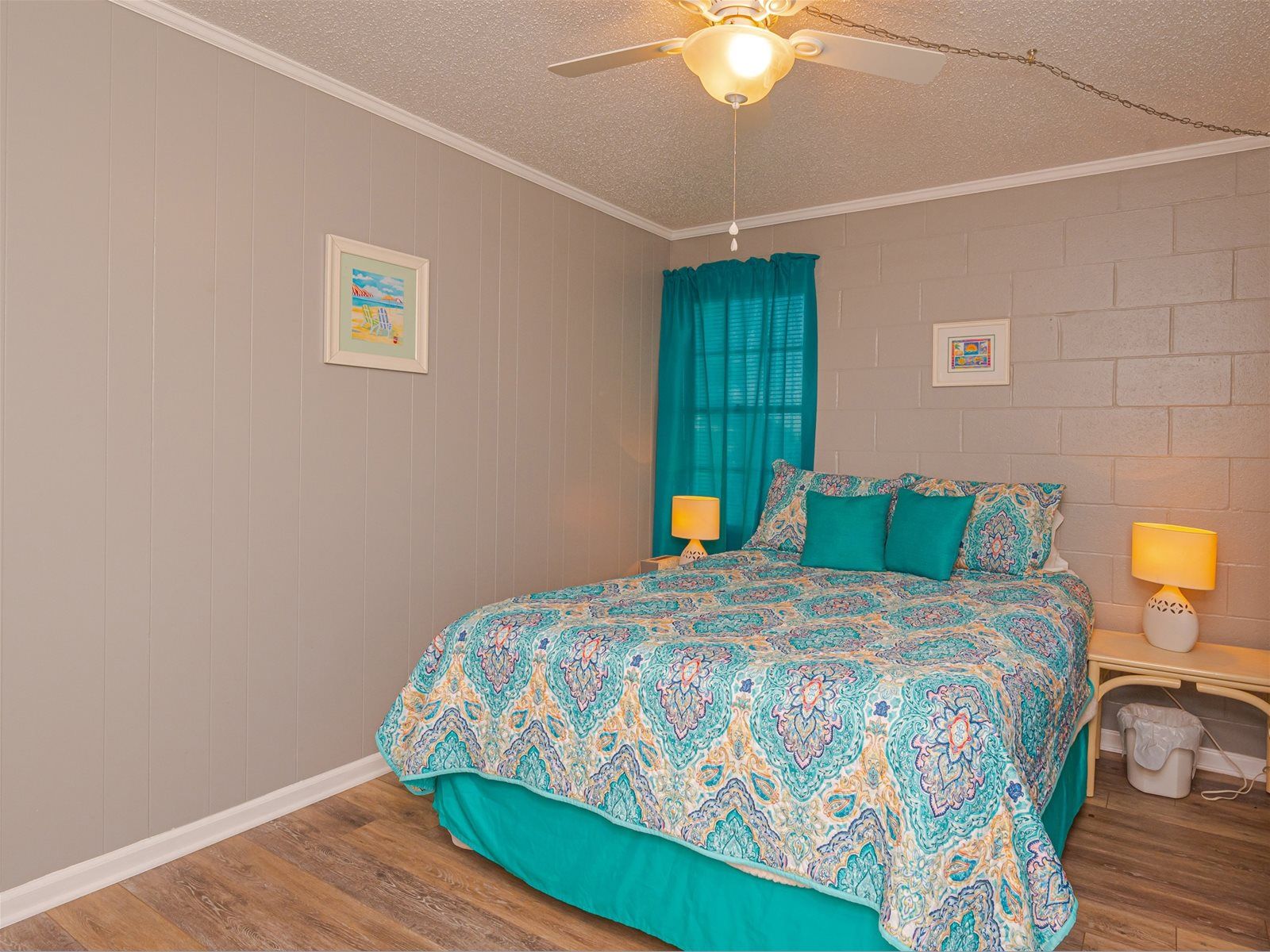 A bedroom with a patterned bedspread, teal curtains, and a ceiling fan.