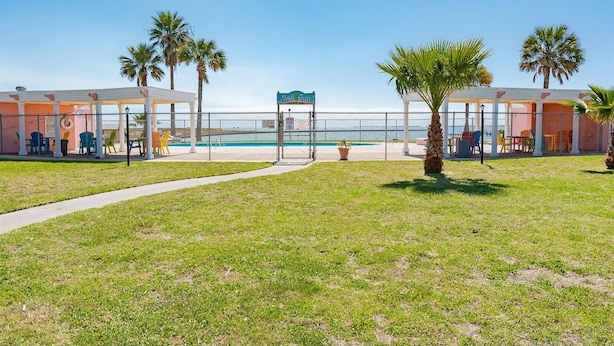 Un hotel frente a la playa con piscina, palmeras y zonas de estar al aire libre.