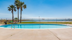Piscina con vista a la playa y al océano, rodeada de palmeras y una valla.