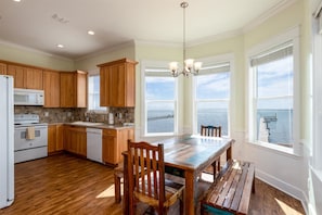 A kitchen with wooden cabinets, a white stove, and a view of the sea through large windows. - Sea Forever by Miss Kitty’s (Rockport)
