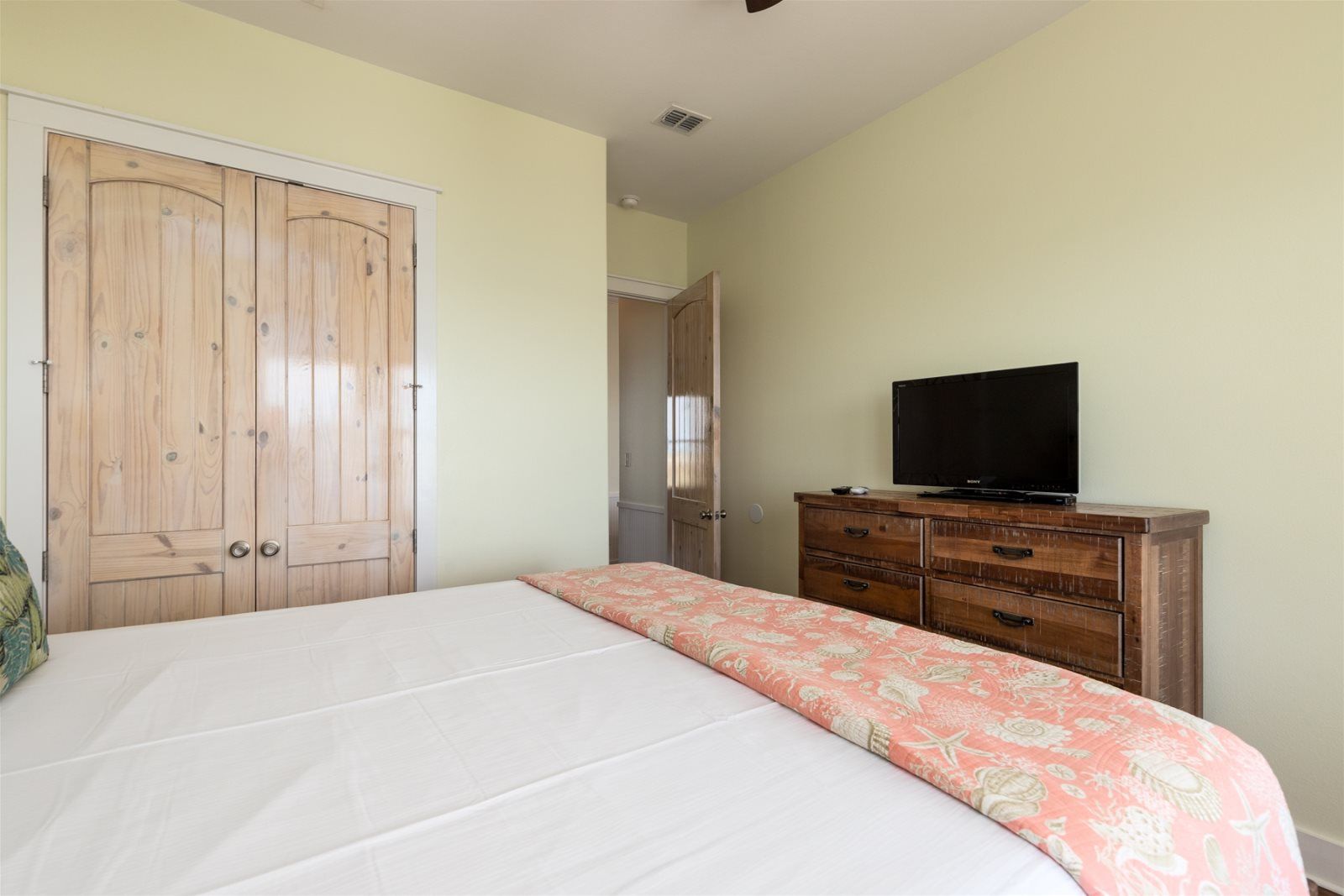A bedroom with a bed, wooden wardrobe, and a TV on a dresser.