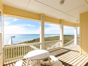 A covered outdoor area with a wooden deck, white railings, and a table with chairs. - Sea Forever by Miss Kitty’s (Rockport)
