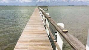 A wooden pier extending into calm water, with a railing on one side and a bench at the end.