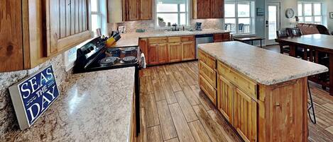 A spacious kitchen with wooden cabinets, a granite countertop, and a sign that reads 'SEAS THE DAY'.