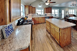 A spacious kitchen with wooden cabinets, a granite countertop, and a sign that reads 'SEAS THE DAY'.