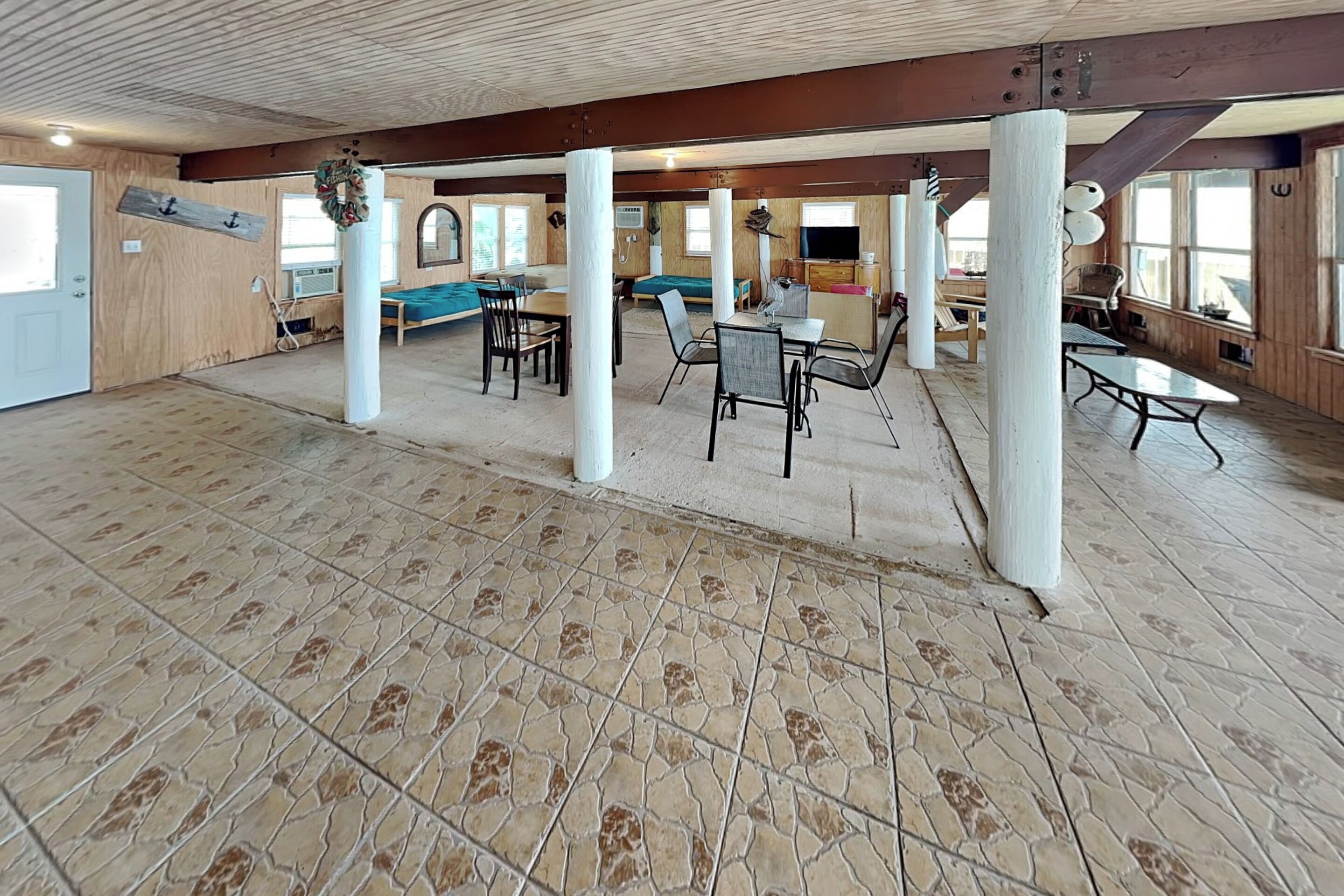 A spacious room with a high ceiling, wooden beams, and a tiled floor.