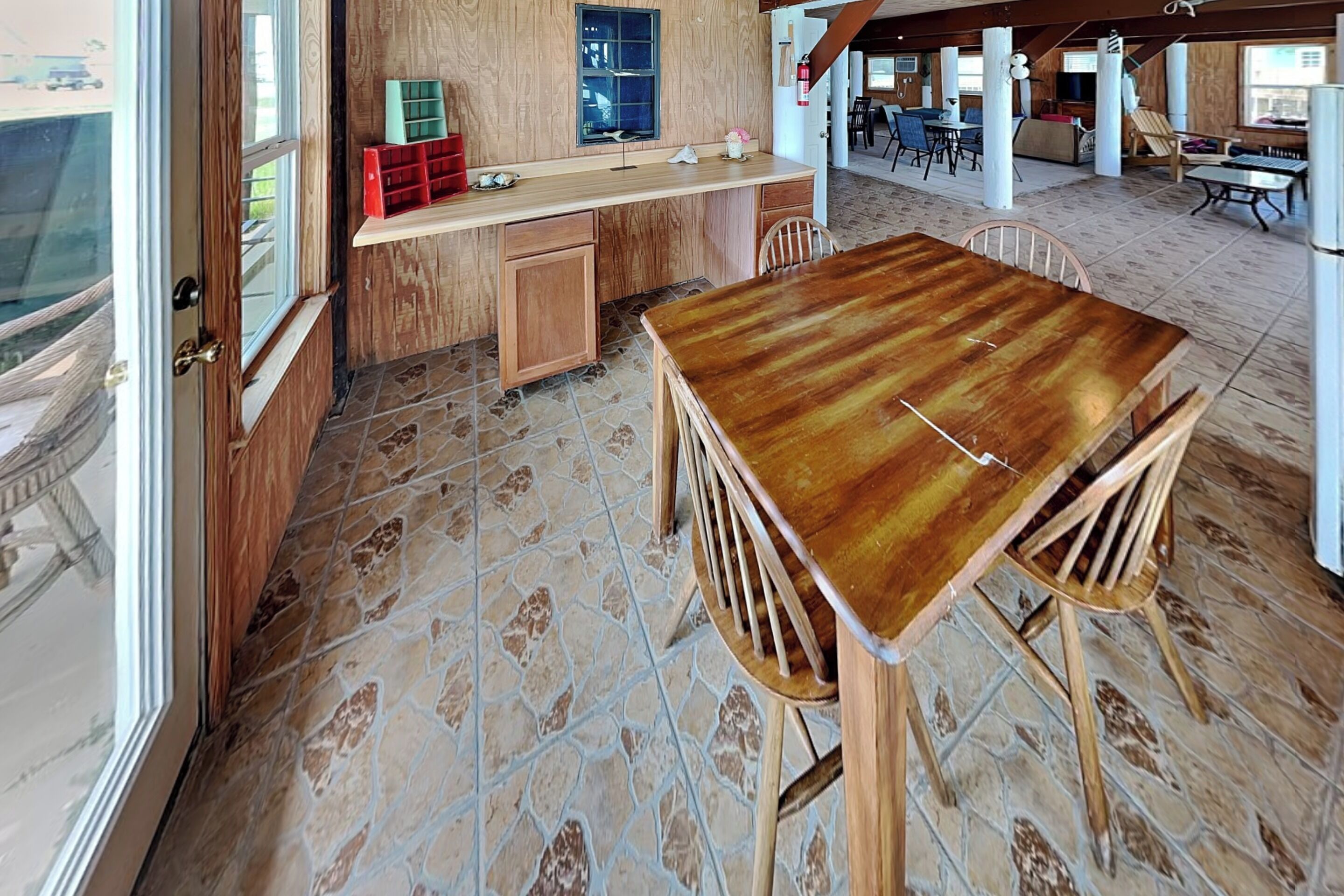 A wooden dining table with chairs, a kitchen area with cabinets, and a stone-tiled floor.