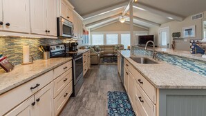 A spacious kitchen with high ceilings, a central island, and a dining area with a sofa. - Sea-esta by Miss Kitty’s (Rockport)