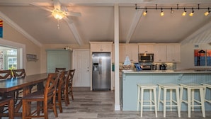 A kitchen with a central island, stainless steel appliances, and a dining area with wooden chairs. - Sea-esta by Miss Kitty’s (Rockport)