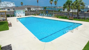 A rectangular swimming pool with clear blue water, surrounded by a wooden fence, and shaded by palm trees. - Sea-esta by Miss Kitty’s (Rockport)
