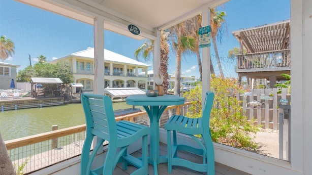 A covered outdoor area with turquoise chairs and a table, overlooking a marina with boats and a building in the background. - Sea-esta by Miss Kitty’s (Rockport)
