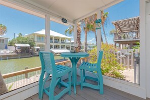 A covered outdoor area with turquoise chairs and a table, overlooking a marina with boats and a building in the background. - Sea-esta by Miss Kitty’s (Rockport)