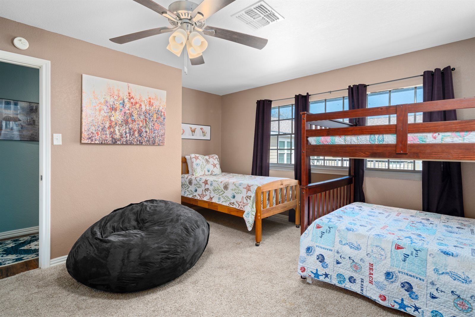 A bedroom with bunk beds, a bean bag, a ceiling fan, and a large window with curtains.